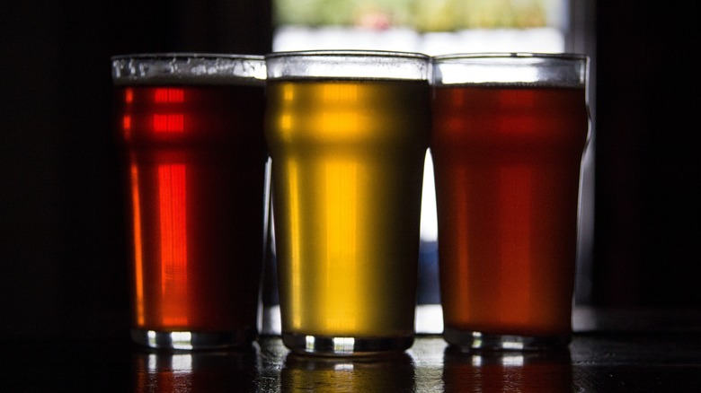 Three glasses of different colored ales in front of a dark background
