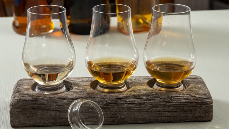 Three glasses on a wood tray, each filled with Scotch or whiskey from a tasting