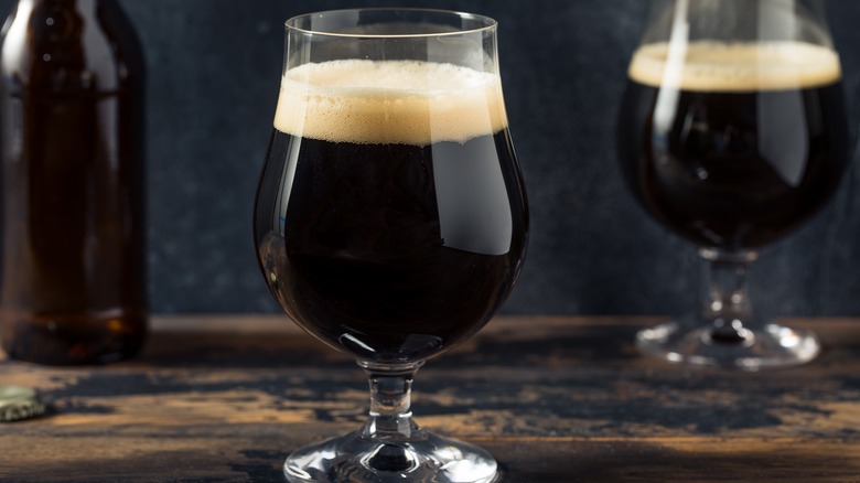 Glass of dark beer with foam on wood table with another glass of beer in back