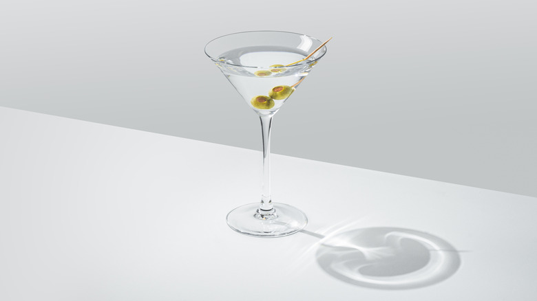 Martini in glass with olive garnish, on white table, with light emphasizing glass' shadow