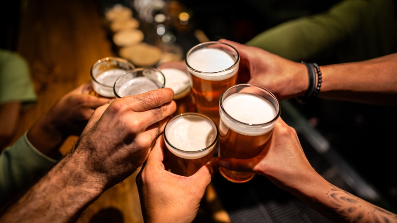 The hands of several people holding beer glasses and toasting