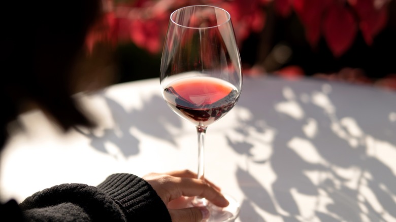 Burgundy wine in glass on white tablecloth with hand touching the base of the glass