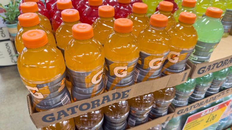 Bottles of orange Gatorade stacked next to other Gatorade colors at a market