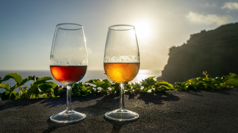Two wine glasses with two different types of Madeira wine on a table outdoors at sunset