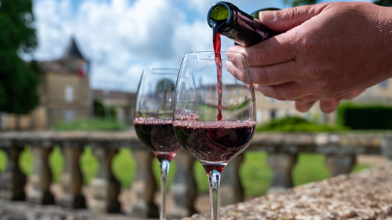 Man pouring French red wine into glass next to another glass of wine