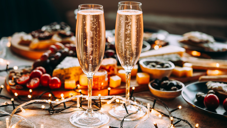 Two tall glasses of champagne surrounded by white Christmas lights and food