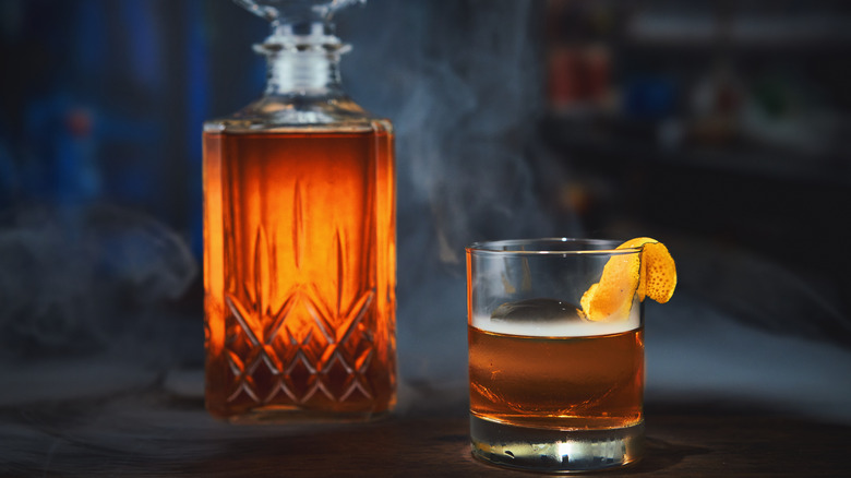 A crystal decanter full of whiskey next to a glass of whiskey on a dark background