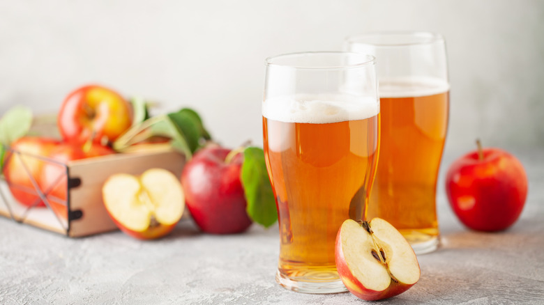 Two glasses of hard cider beside cut and whole apples
