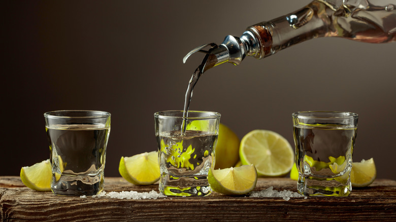 A bottle of tequila pouring into shot glasses.