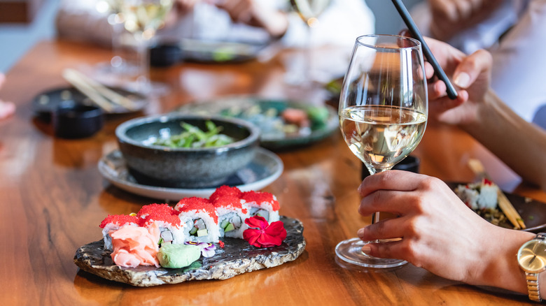 Hand holding a glass of wine next to a platter of sushi