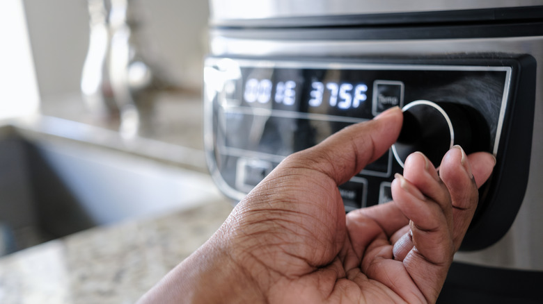 A person's hand is seen turning the dial on an air fryer.