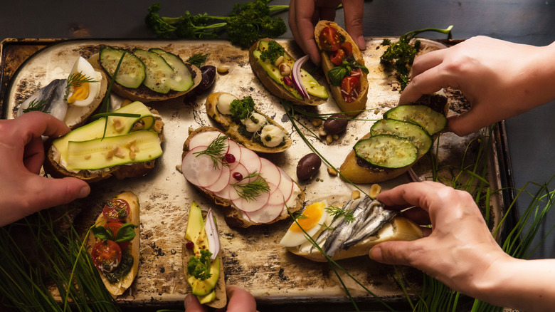 Hands reaching for an assortment of open faced sandwiches