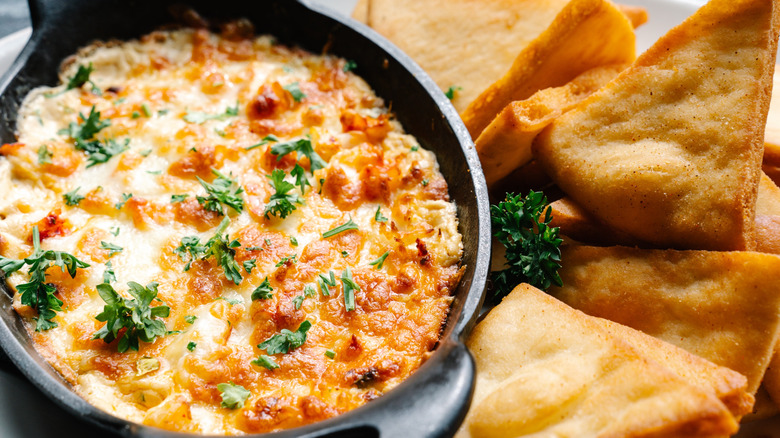 A decadent, cheesy lobster dips is pictured in close up beside pita chips.