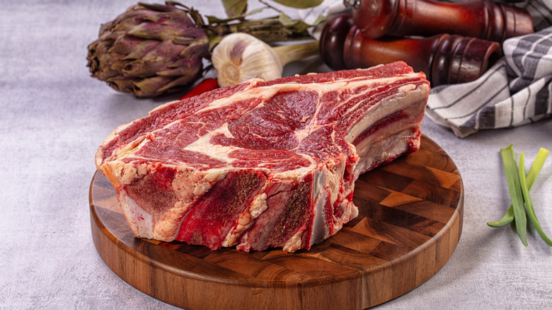 A raw bone-in prime rib displayed on a circular cutting board