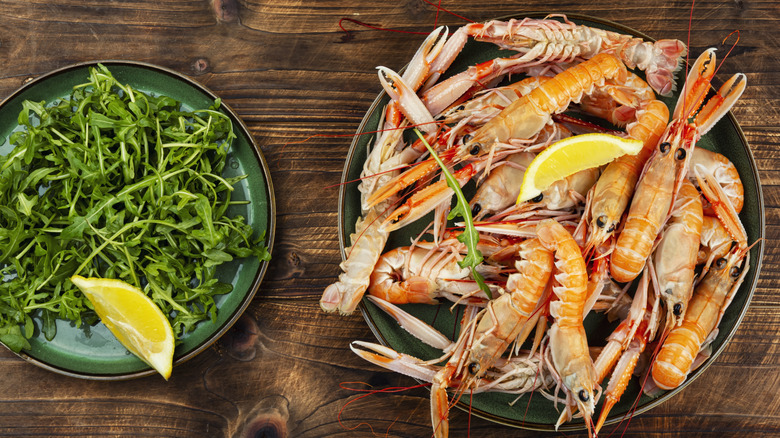 A big dish of whole langostinos beside a plate of arugula.