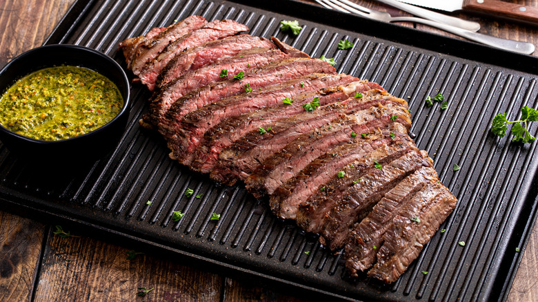 A large, sliced skirt steak rests on a tray on a wooden table.