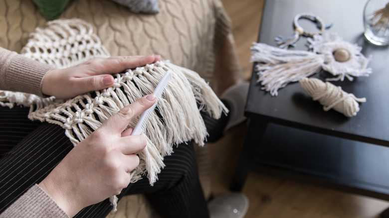 A woman combs the fringe on a macrame hammock.