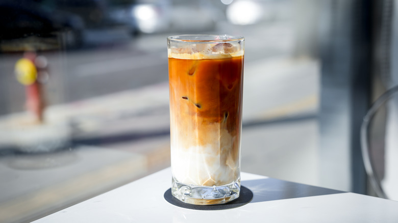 An iced latte on a black coaster that is on a white table