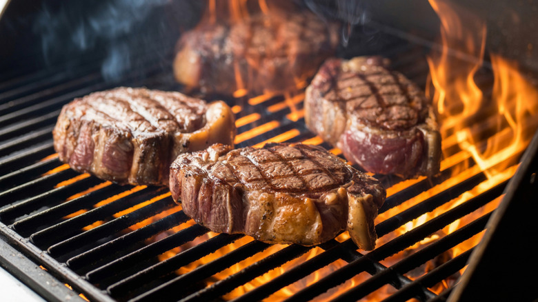 Ribeye steaks cooking on a flaming grill