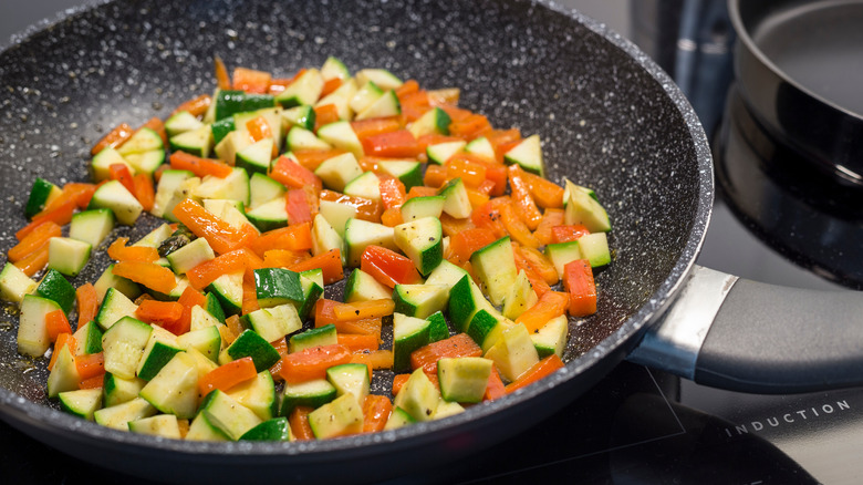Zucchini and peppers sautéing in a frying pan 