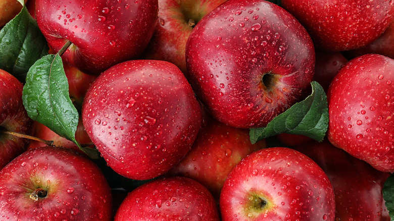 A pile of red apples covered with water droplets, with some green leaves here and there