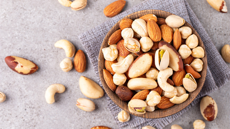 Mixed nuts in a bowl with several spilling onto the tabletop