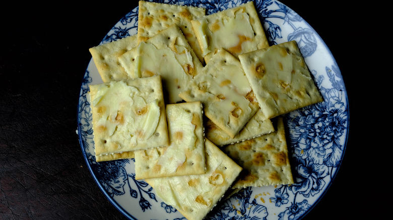 A blue plate filled with buttered Saltine crackers on a black background
