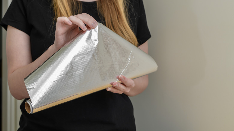 A woman holds a roll of aluminum foil