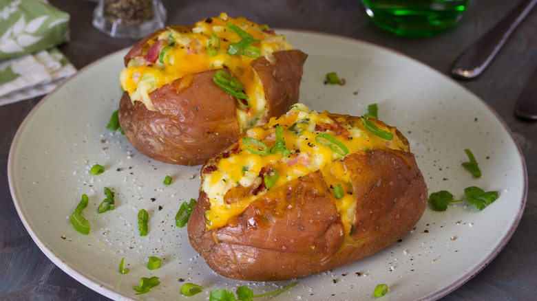 Baked potatoes on a white plate topped with cheese, bacon, and green onions