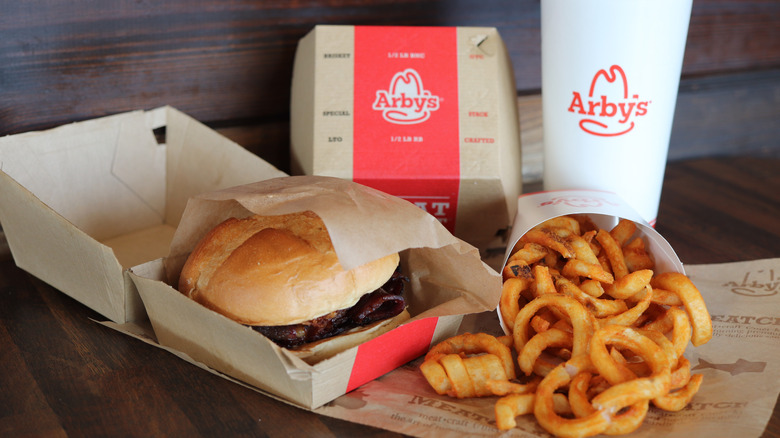 Arby's sandwich, curly fries, box, and a drink on a table