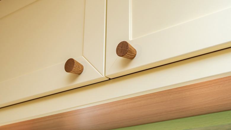 Natural wood knob handles on beige kitchen cabinet.