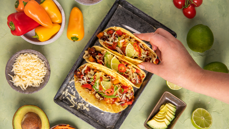 A hand reaches for a trio of tacos