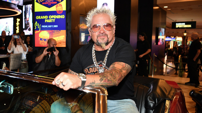 Guy Fieri sits atop a red convertible at a grand opening event