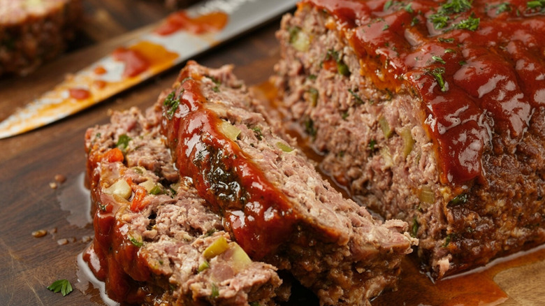 A meatloaf with two slices already cut on a cutting board