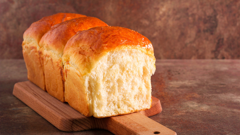 A fluffy loaf of bread is pictured on a wooden cutting board.