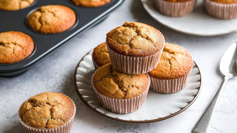 Homemade muffins in a muffin pan and three muffins stacked on a plate