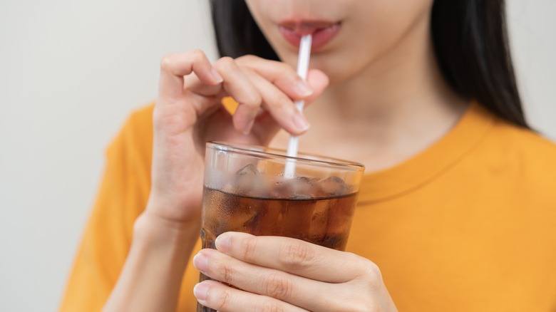 Person sipping a glass of iced cola