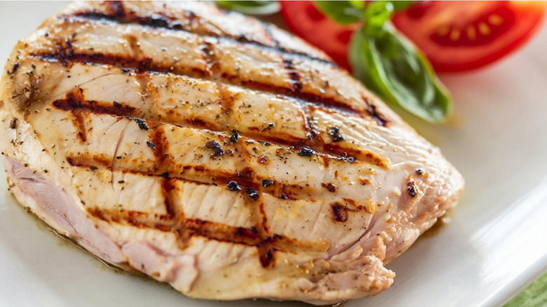 Juicy grilled chicken breast on a plate with tomato and basil