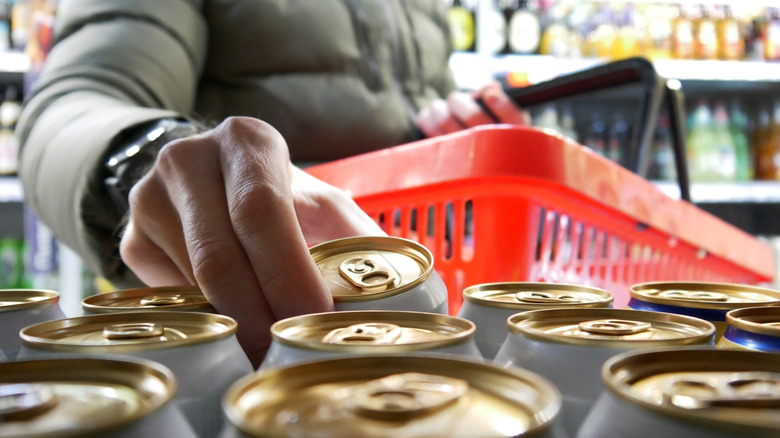 A person's hand reaches for a single can of beer in a store.