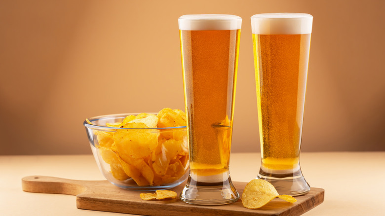 Two crisp lager beers with foam and a side of potato chips
