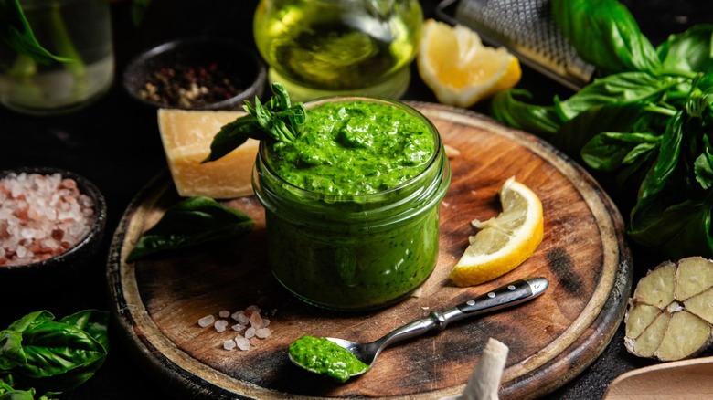 A jar of bright green fresh pesto with basil sticking out of it and a spoon with pesto on it sitting to the side.