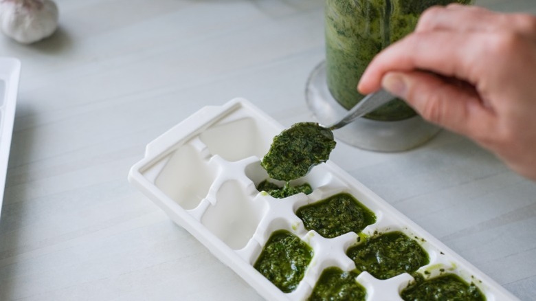 A person filling an ice tray with spoonfuls of fresh pesto to freeze it and make it last for months.