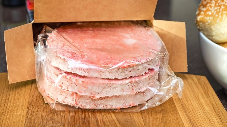 A package of frozen burger patties partially slid out of a cardboard box on a wooden counter surface.