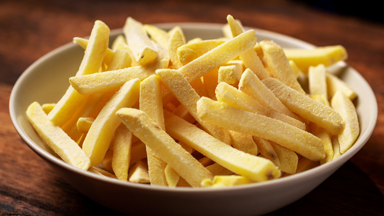 Small beige bowl of frozen fries on a wooden table