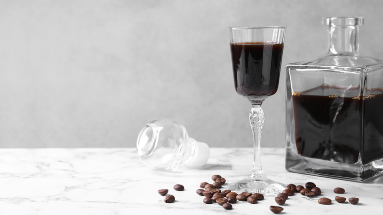 Homemade coffee liqueur in glass bottle next to small glass on white counter.