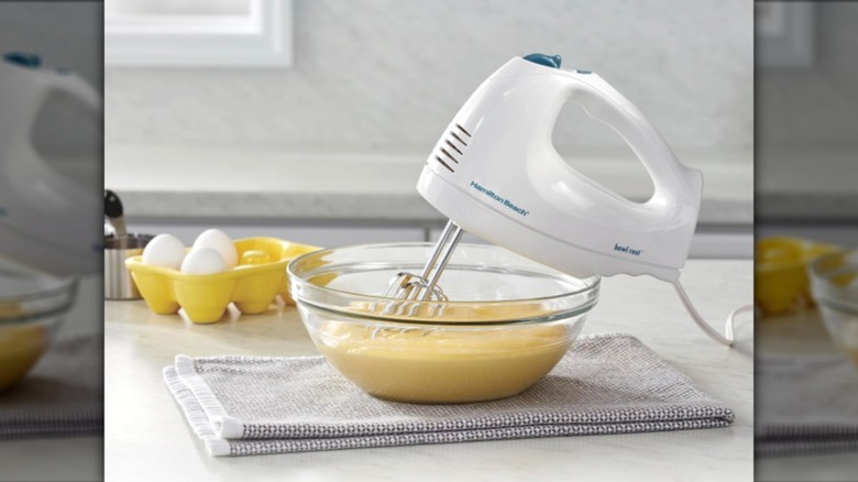 Hamilton Beach 6-speed hand mixer resting with the beaters in a clear bowl of yellow batter