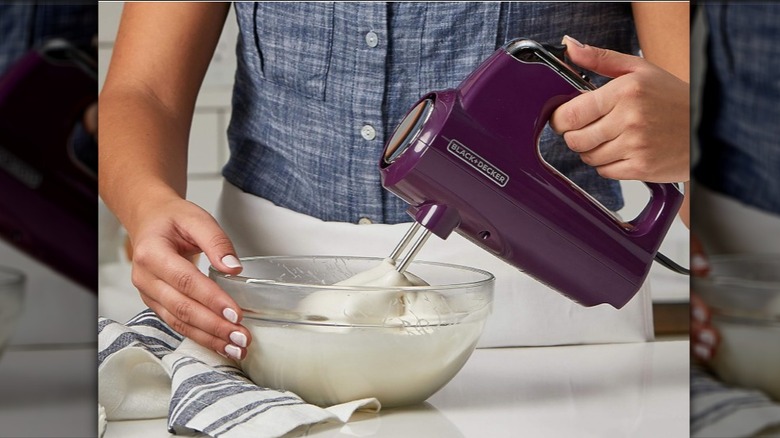 Person using the purple Performance Helix Premium Hand Mixer on a bowl with white batter