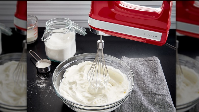 KitchenAid 9-Speed Hand Mixer poised with its whisk attatchment just touching a bowl full of whipped cream