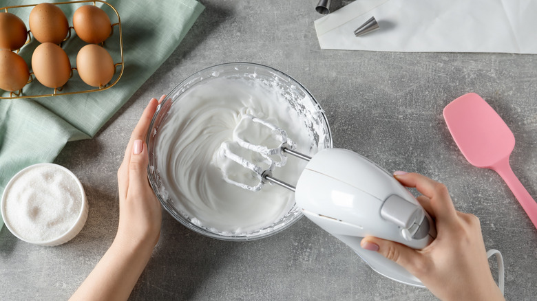Person whipping egg whites and sugar in a bowl with a hand mixer