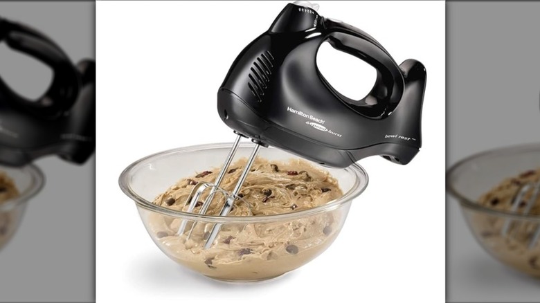 Black Hamilton Beach Power Delux 6-Speed Hand Mixer with beaters in a clear bowl of chocolate chip dough on a white background
